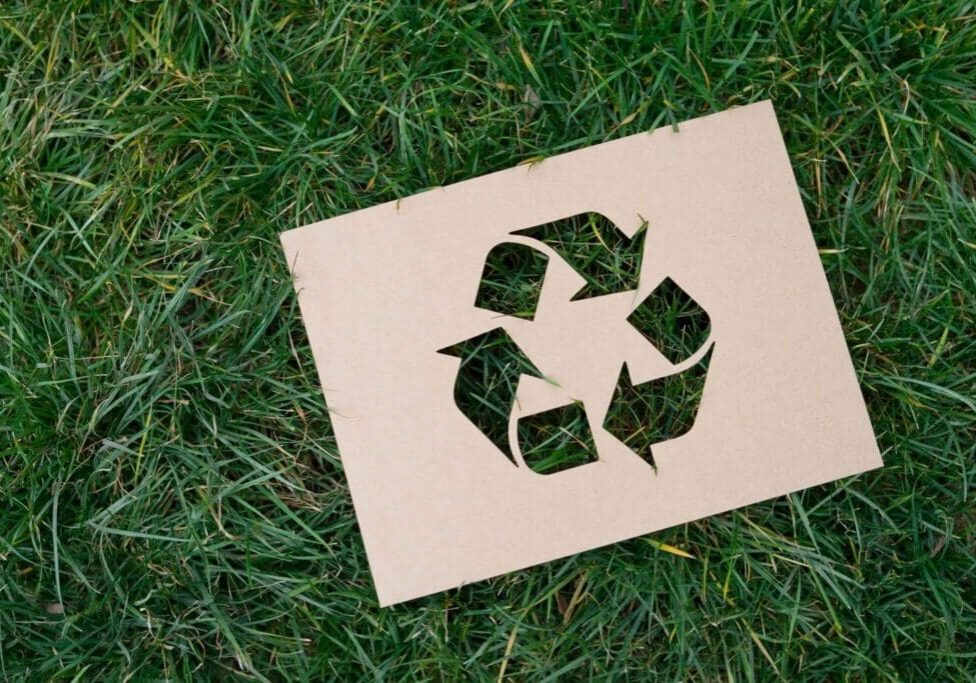 A cardboard cut out of the recycling symbol on grass.